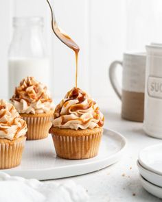 three cupcakes with frosting being drizzled onto them on a plate