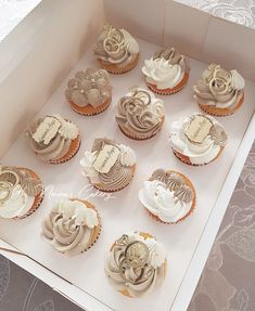 twelve cupcakes in a box with white frosting and decorative designs on them