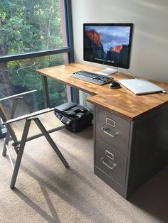 a desk with a computer on top of it in front of a window overlooking the trees