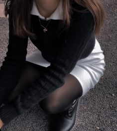 a woman sitting on the ground with her hands in her pockets, wearing black and white tights