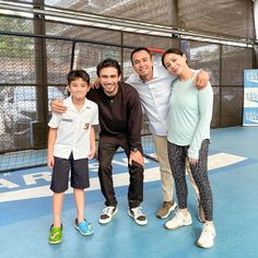 a group of people standing next to each other on a tennis court with net in the background