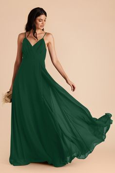 a woman in a long green dress is holding a straw bag and looking at the camera