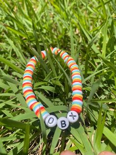 a hand holding a beaded bracelet with two letters on it in the middle of some grass