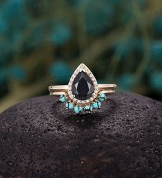 a black diamond and turquoise gems ring on top of a rock in front of some rocks