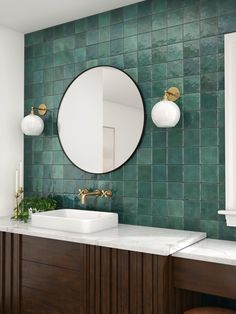 a bathroom with two sinks and a round mirror on the wall above it is green tile