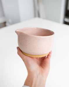 a hand holding a pink bowl on top of a white table