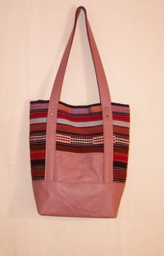 This tote is made from multicolored handwoven North African fabric in cotton and wool with dusty rose leather base and straps. It has a heavy deep red Bursa silk lining with one inner zipper pocket, an exterior pocket and a magnetic clasp. It measures 14" x 14" with 28" handles. Multicolor Handwoven Leather Shoulder Bag, Multicolor Leather Handwoven Shoulder Bag, Handwoven Multicolor Leather Shoulder Bag, Multicolor Handwoven Leather Bags, Handwoven Multicolor Leather Bags, Pink Leather Bag With Leather Trim, Everyday Handwoven Leather Bags, Pink Satchel Bag With Leather Trim, Pink Bags With Leather Trim For Daily Use