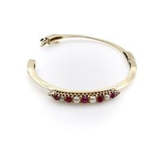 This is part of Chairish’s Fine Jewelry assortment.  The centrepiece of this charming bracelet was most likely once a brooch, converted at some point into a stylish bangle. It contains six round half pearls and five oval-shaped cabochon rubies, prong-set into an alternating pattern, that has been beautifully incorporated into a knife edge bracelet. Each end of the bar culminates in triangular points, which marry into the knife edge for a clean and sophisticated look. The 14k gold bangle has a sa Elegant Cabochon Bracelets For Anniversary, Elegant Multi-stone Cuff Bangle Bracelet, Elegant Cabochon Bracelet Jewelry, Elegant Multi-stone Bangle For Anniversary, Antique Multi-stone Bracelet For Formal Occasions, Antique Multi-stone Bracelets For Formal Occasions, Yellow Gold Cabochon Bracelets For Weddings, Elegant Oval Hallmarked Bangle, Elegant Formal Cabochon Bracelets