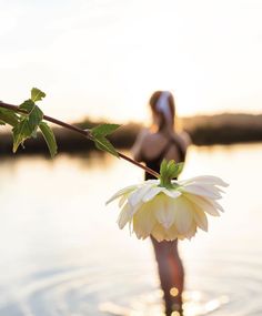 a woman is standing in the water with a flower hanging from her arm and behind her back