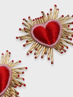 two red and gold heart shaped brooches with spikes on each side, set against a white background