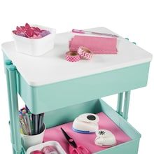 a small table with some craft supplies on it and a bowl of pink flowers in the background