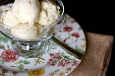 two scoops of ice cream in a glass bowl on a floral plate with a spoon