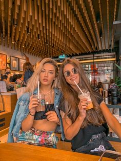 two beautiful young women sitting next to each other holding drinks