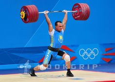 a man lifting a barbell in front of a blue wall with the olympic logo on it