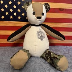 a teddy bear sitting on top of a bed next to an american flag and wooden wall