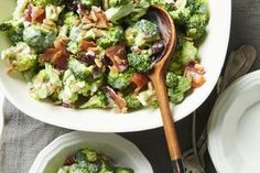 broccoli salad with bacon in a white bowl and serving utensils on the side