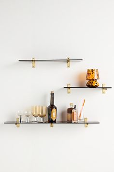 two shelves with wine glasses, bottles and candles on them in front of a white wall