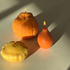 two oranges and an apple sitting on a table next to each other in the sunlight