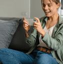 a woman sitting on a couch looking at her cell phone while holding something in her hand