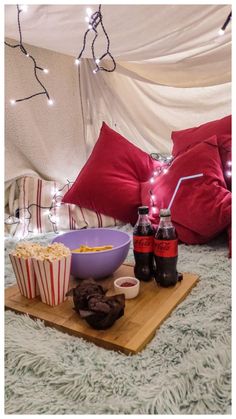 some food and drinks on a tray in front of a bed with lights strung up over it