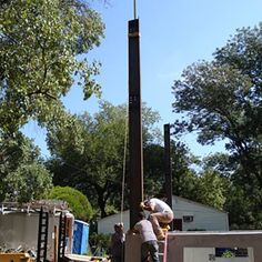 two men working on a tall pole in the middle of a yard next to trees