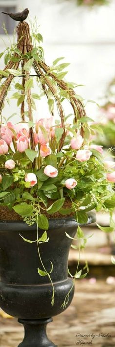 some pink flowers are hanging from a planter in front of other potted plants