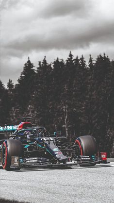 a racing car driving on a track with trees in the background and dark clouds overhead