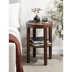 a small round wooden table with two books on it next to a white couch and plant