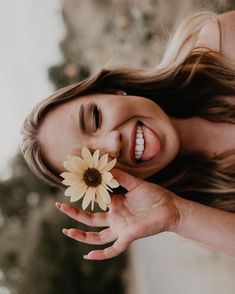 a woman is smiling and holding a flower in her hand while she looks at the camera