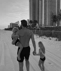 a man and two children walking on the beach in front of high rise buildings with palm trees