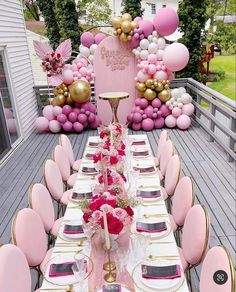 a table set up for a party with balloons and flowers on the table, along with pink chairs