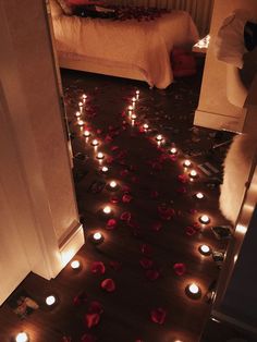 the floor is covered with candles and rose petals in front of an open door that leads to a bed