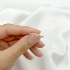 a woman's hand holding a diamond ring on top of a white cloth background