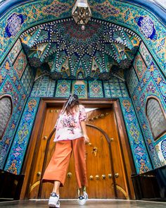 a woman standing in front of a wooden door with ornate designs on the doors and walls