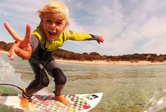 a young boy riding a surfboard on top of a wave in the ocean with his fingers up