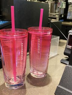 two pink tumblers sitting on top of a counter next to each other with straws in them