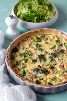 a broccoli and chicken quiche in a white dish next to a salad