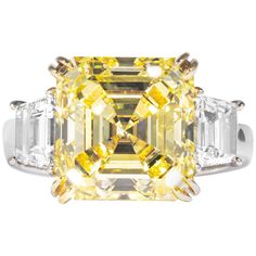 This fancy yellow square emerald cut diamond is offered by Shreve, Crump & Low. This fancy yellow square emerald cut diamond is custom set in a handcrafted Shreve, Crump & Low platinum and 18 karat yellow gold 3 stone ring consisting of 1 square emerald cut yellow diamond weighing 7.03 carats with color and clarity of Fancy Yellow VS1 accompanied by GIA report No. 10237242, accented by 2 trapezoid shaped diamonds with a total weight of approximately 1.22 carats, and a respective color and clarity of D-F VS1-VS2 quality. The setting is a ring size 6.5, and is stamped with our maker's hallmark "SC&L" "PLAT" "18k" on inside of ring shank. Shreve, Crump & Low is one of America's oldest and most prestigious jewelry and fine gift establishments founded in 1796. Shreve, Crump & Low has storefront Square Cut Diamond Ring, Canary Diamond Ring, Square Cut Rings, Radiant Diamond Rings, Canary Diamond, Emerald Cut Diamond Ring, Moissanite Diamond Rings, Emerald Cut Diamond, Radiant Diamond