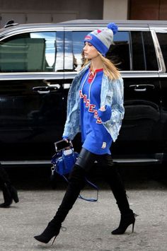 a woman walking down the street wearing black boots and a blue jacket with red letters on it