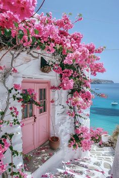 pink flowers are growing on the side of a white building with a pink door and window