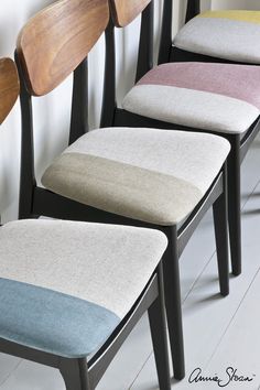 four wooden chairs with different colored cushions on the seat and backrests are lined up against a white wall