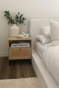 a bed with white sheets and pillows next to a night stand on top of a wooden floor