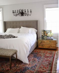 a bed with white sheets and pillows on top of it next to a rug in front of a window