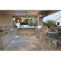 an outdoor kitchen with stainless steel appliances and lights on the counter tops, along with a pool in the background