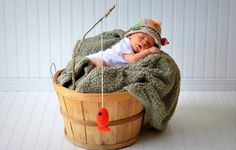 a baby wrapped in a blanket is laying in a basket with a toy fish hanging from it's side