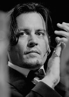 a man in a suit and tie holding his hand up to his ear while looking off into the distance