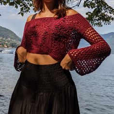 a woman standing next to the water wearing a red knitted top and black skirt