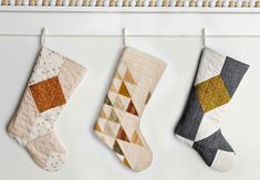 three christmas stockings hanging from hooks on a white wall, one with an argyle pattern and the other with geometric shapes