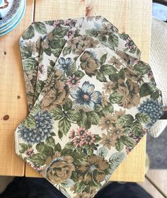 four floral printed napkins sitting on top of a wooden table next to a plate