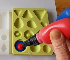 a hand is holding a red marker near an ice tray with holes and shapes on it